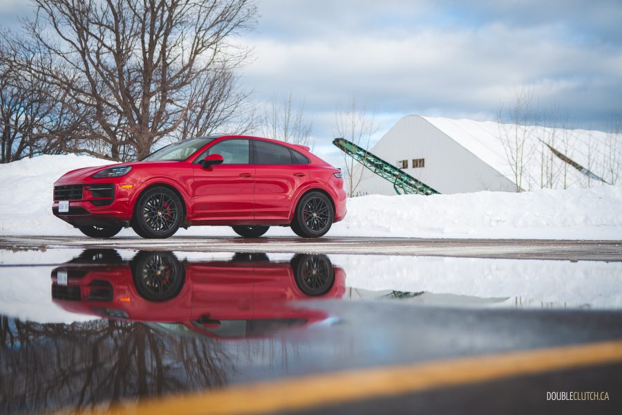 Front three quater view of the 2025 Porsche Cayenne GTS in Carmine Red with reflection off water