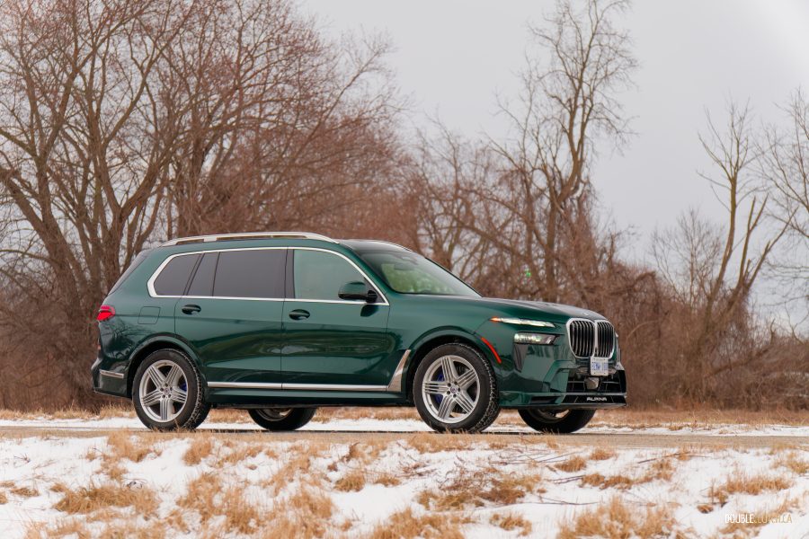 Front quarter view of a green 2025 BMW Alpina XB7 in a parking lot with trees in the background